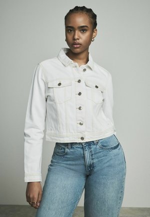 White denim cropped jacket with two chest pockets, silver buttons, and visible stitching. Paired with light blue high-waisted jeans.