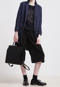 Navy oversized blazer, black lace top, wide black culotte pants, and black leather shoes. Black structured handbag with short handles.