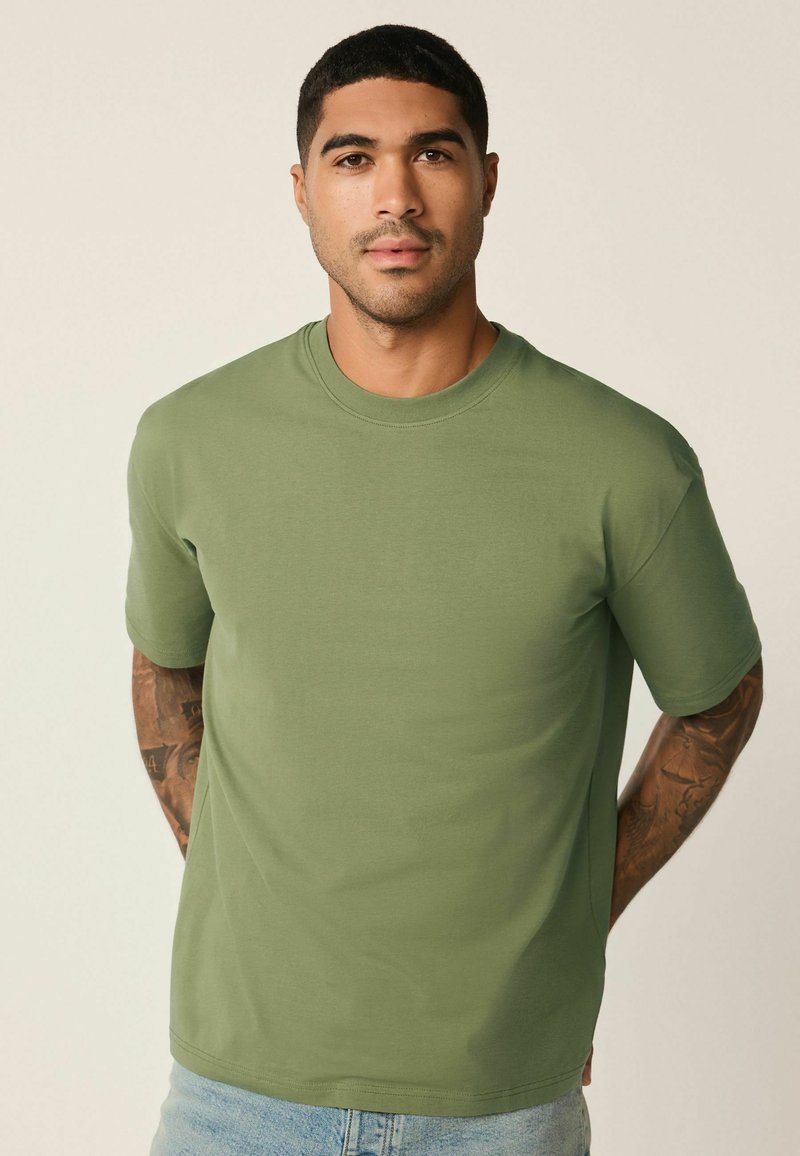 Oliivinvihreä lyhythihainen t-paita pyöreällä pääntiellä, valmistettu pehmeästä jerseymateriaalista. Siinä on rento istuvuus ja sileä, matta viimeistely.