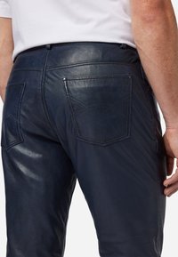 Marineblauwe leren broek met een gladde textuur. Heeft achterzakken met subtiele stiksels. Aansluitend design met een eenvoudige tailleband.