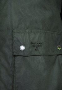 Dark green jacket featuring a flap pocket with a silver snap button, embroidered "Barbour" logo, and subtle texture.