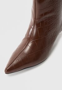 Botte de cheville en cuir brun embossé de crocodile avec un bout pointu et un design élégant, présentant une texture lisse et des détails de couture subtils.
