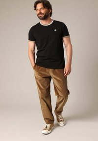 T-shirt en coton noir avec col et poignets blancs, assortie à un pantalon en velours côtelé marron et des baskets beiges, dotées de lacets et d'accents contrastants.