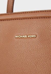 Ruskean tekstuurin omaava synteettinen nahkabag, jossa on kultainen "MICHAEL KORS" -logo selvästi esillä. Saumat ovat huomaamattomat reunoilla.