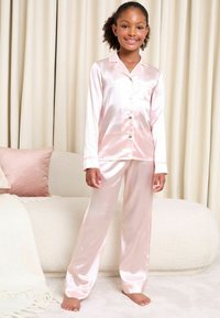Súprava pyžama v svetloružovej saténovej farbe, s dlhými rukávmi, zapínaním na gombíky a zodpovedajúcimi nohavicami. Hladká textúra s klasickým dizajnom goliera.
