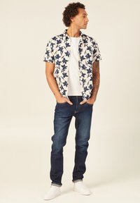 Valkoinen lyhythihainen paita, jossa on tummansiniset kukkakuviot, yhdistettynä tummansiinisiin farkkuihin ja valkoisiin lenkkitossuihin. Paita on väljää mallia.