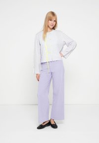 Cropped gray checkered jacket with yellow ties, paired with lilac wide-leg striped pants. Black flats complete the outfit.