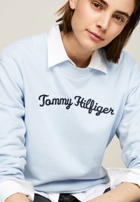 Felpa azzurra in cotone con scollatura rotonda. Presenta la scritta "Tommy Hilfiger" ricamata in corsivo blu scuro.