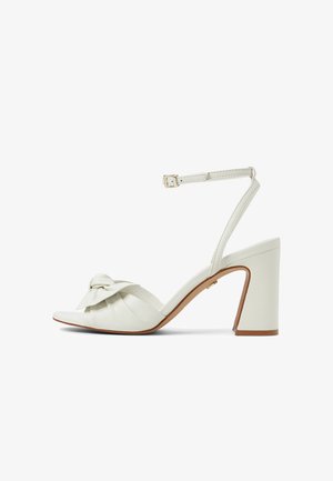 Sandale à talon haut en cuir blanc avec bride à la cheville et boucle, détail noué à l'avant-pied, et talon bloc avec bords de semelle couleur fauve.