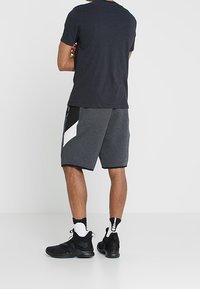 Pantalones cortos deportivos grises con un diseño de triángulo blanco en contraste; combinados con zapatillas negras y calcetines de estampado; camiseta negra de manga corta lisa.