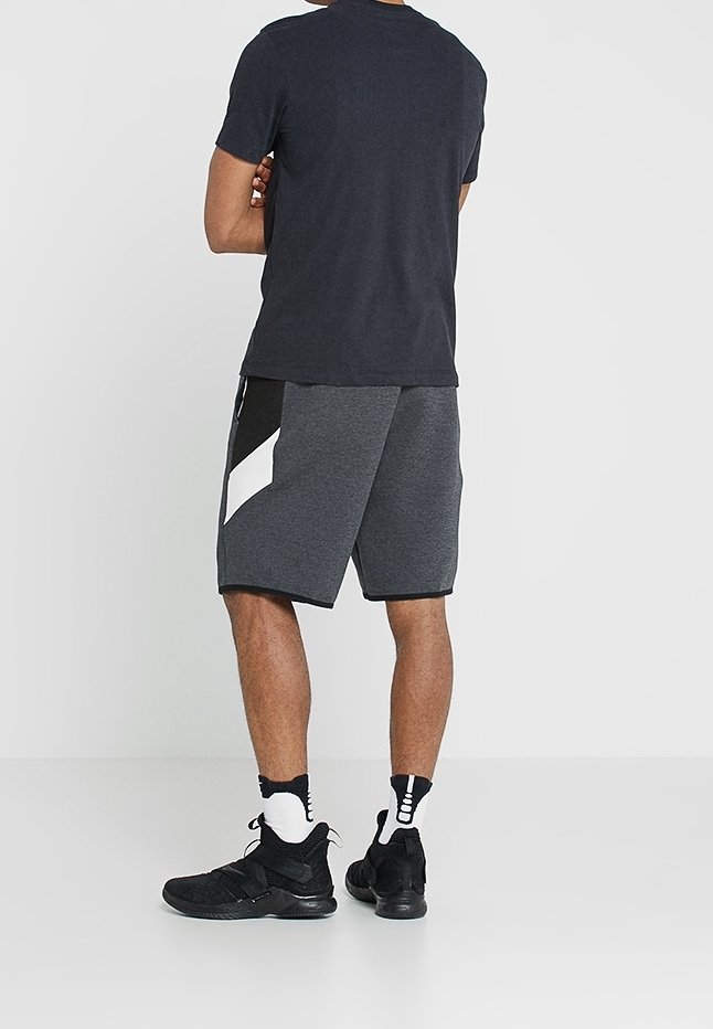 Pantalones cortos deportivos grises con un diseño de triángulo blanco en contraste; combinados con zapatillas negras y calcetines de estampado; camiseta negra de manga corta lisa.