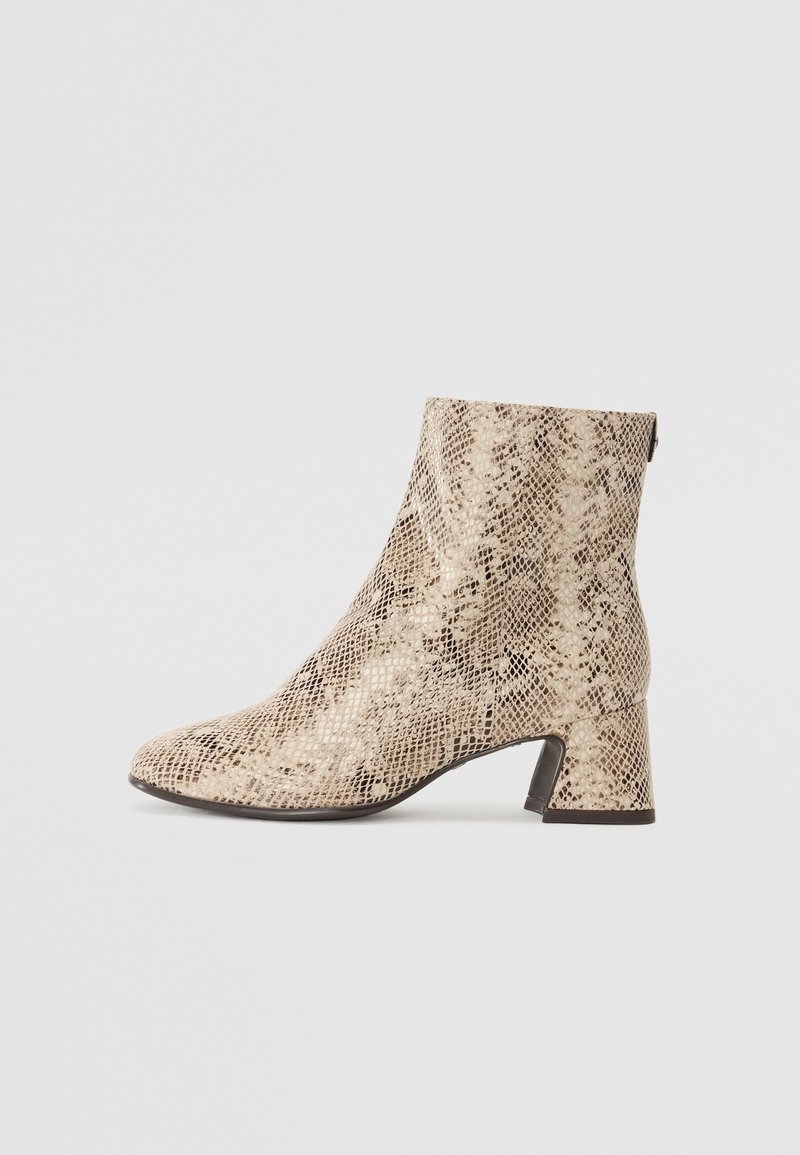 Bottine beige à motif serpent, talon bloc et fermeture éclaire latérale, présentée sur un fond clair uni.