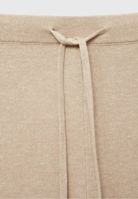 Ceinture en tissu tricoté beige avec un cordon plat noué au centre avant, montrant des coutures détaillées et la texture.