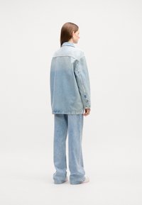 Veste en denim bleu clair au fit légèrement oversize, avec un col classique et des poignets boutonnés, assortie à un pantalon large.