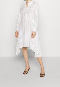 Abito camicia bianco a maniche lunghe con righe verticali blu navy, con bottoni, orlo curvo e lunghezza alla caviglia; abbinato a tacchi con stampa leopardata.