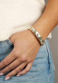 Guldarmband med fem klara ädelstenar i en elegant, böjd design. Slät yta med en polerad finish.