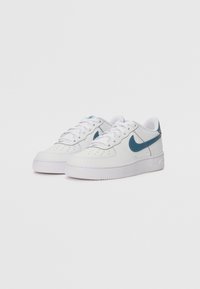 Bijele kožne tenisice s glatkom teksturom, koje imaju tirkizni Swoosh, vezivanje na vezice i ravni gumeni potplat. Naglašeni detalji šivanja.