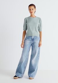 Pull court à manches courtes vert clair avec une finition texturée, associé à un jean en denim bleu clair oversize. Les jeans ont une coupe décontractée.