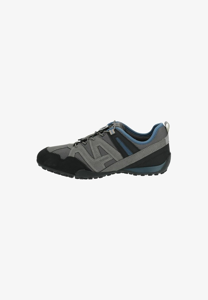 Zapatilla deportiva en tonos gris y negro, con paneles de malla, acentos texturizados, una puntera redondeada y una suela de goma con un patrón de agarre.