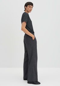 T-shirt gris scintillant à manches courtes associé à un pantalon large. La tenue présente une coupe décontractée et un tissu texturé, avec des poches sur les côtés.