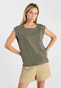 Haut sans manches vert olive avec un décolleté carré, doté de accents en métal argenté et d'un design simple. Accompagné de shorts beiges.