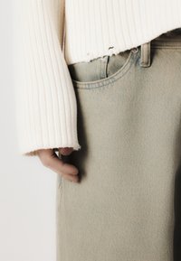 Ribbete, kremfarget genser med bred ermfald, kombinert med lysegrønne denimjeans som har en frontlomme og subtilt teksturert mønster.