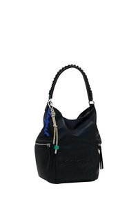 Bolso de mano negro de piel sintética con forma caída, asa trenzada, detalles con cremallera y un llavero azul de "Desigual" como acento. Logo embellecido sutilmente.