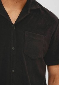 Camicia nera a maniche corte realizzata in tessuto texture, con chiusura a bottoni sul davanti e taschino sul lato sinistro del petto. Design del colletto classico.