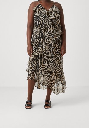 Mujer con vestido midi sin mangas con estampado de cebra en negro y beige con detalles de volantes y sandalias negras de punta abierta con hebillas.