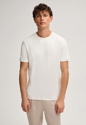 White, short-sleeve t-shirt made of soft fabric with a round neckline and subtle embossed logo on the chest. Paired with light beige pants.