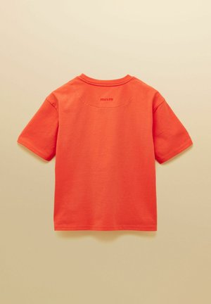 Spilgti oranža īsroku t-krekls, redzams no aizmugures, ar nelielu "SOU·LES" tekstu pie kakla uz bēša fona.