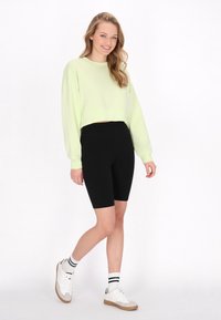 Felpa verde chiaro a maniche lunghe e cropped, abbinata a pantaloni corti biker neri. Sneakers bianche con suole marroni e calze a righe nere.