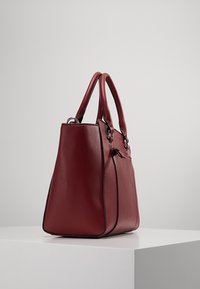 Czerwona skórzana torba o wyraźnym, usztywnionym kształcie, z dwoma uchwytami i zamkiem błyskawicznym. Charakteryzuje się gładką fakturą oraz subtelnymi przeszyciami wzdłuż krawędzi.