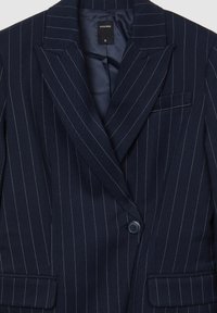 Blazer a righe blu navy in un tessuto strutturato, con chiusura a un bottone, revers a punta e taschino sul petto. Tag della taglia: S.