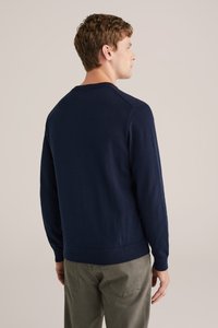 Mornarski pulover z dolgimi rokavi, okroglega izreza in rebrastim robom. Tkanina izgleda pleteno in gladko, z enostavnim dizajnom, brez vidnih vzorcev ali okrasov.