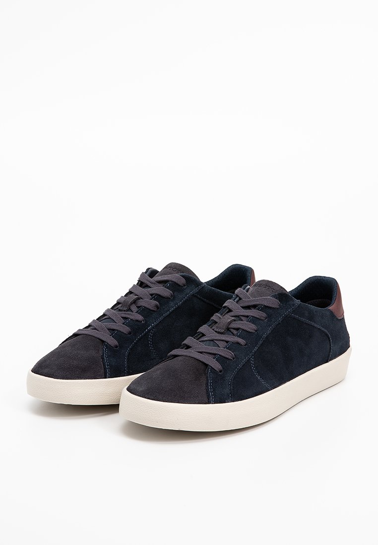 Baskets en daim bleu marine avec des semelles en caoutchouc beige, ornées d'un accent en cuir brun foncé au niveau du talon et de lacets plats.