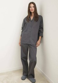 Pijamas grises que cuentan con una parte superior de botón con dos bolsillos frontales y pantalones sueltos a juego. Textura suave, diseño simple y silueta relajada.