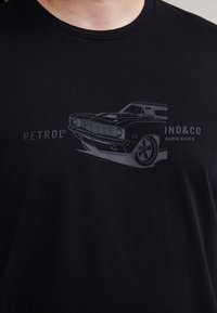 Camiseta de algodón negra con una gráfica de un coche clásico en la parte frontal, con el nombre de la marca "PETROL" y el eslogan "DENIM DRIVEN" debajo.