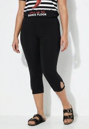 Vrouw draagt zwarte cropped leggings met enkeluitsparingen, zwarte sandalen met gespen en een gestreept shirt met rode tekst "spice up the dance floor."