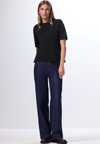 Camiseta negra de manga corta con letras texturizadas; combinada con jeans de tiro alto y pierna ancha en azul oscuro y botas gruesas negras.