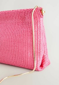 Vaaleanpunainen kudottu clutch-laukku, jossa on tekstuuripinta, kultasävyinen ketjuolkaimet ja vetoketjusuljin ylhäällä.