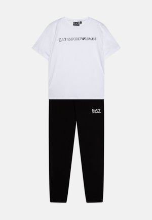 Vit bomull t-shirt med svart text "EA7 EMPORIO ARMANI", kombinerad med svarta bomullsträningsbyxor med en liten vit logotyp på låret.
