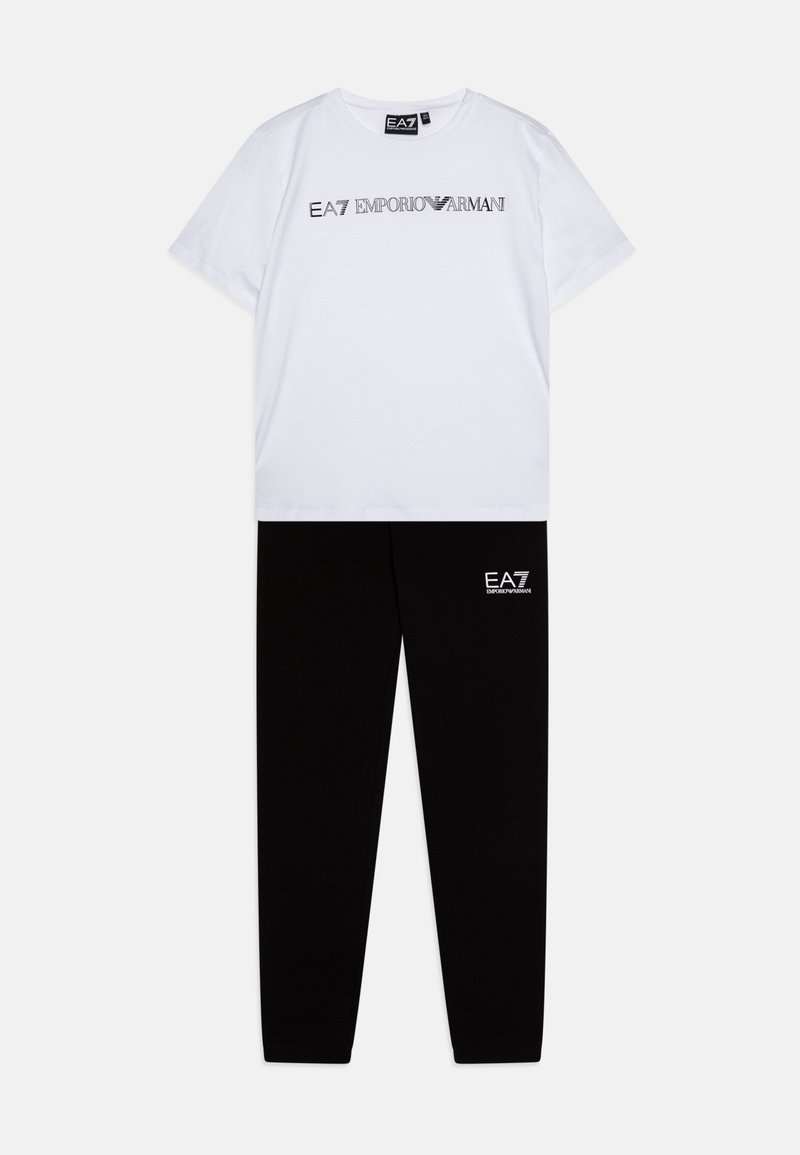T-shirt en coton blanc avec le texte noir "EA7 EMPORIO ARMANI", associé à un pantalon de survêtement en coton noir comportant un petit logo blanc sur la cuisse.