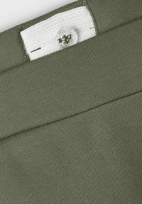 Tessuto verde oliva con superficie testurizzata, caratterizzato da una fascia interna bianca e un dettaglio in plastica trasparente nella zona della vita.