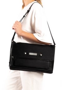 Black leather bag with a long adjustable strap, featuring a zippered front pocket and silver hardware accents. Smooth texture, rectangular shape.