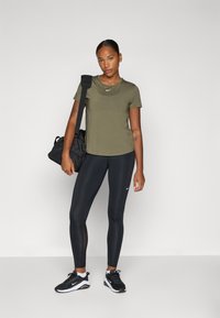 Camisa deportiva de manga corta en verde oliva,leggings negros con paneles de malla, zapatillas negras y una bolsa de gimnasio negra. Diseño simple y atlético.