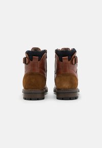 Botas de tobillo de cuero marrón y ante con un acabado texturizado, que cuentan con cierre de cremallera, detalle de hebilla y suelas de goma con ranuras de tracción.