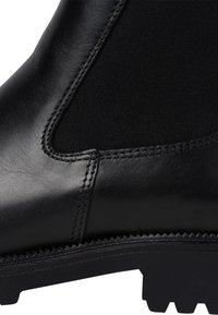 Botín negro de piel con acabado suave, paneles de tela elástica y suela de goma resistente con detalles de agarre texturizados.