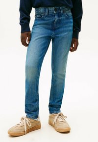 Vaqueros azul desgastados de corte recto, con cinco bolsillos y cierre de botón, combinados con sneakers de ante en color beige claro.