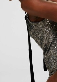 Stříbrné a černé šaty s flitry ve štíhlém střihu, s nastavitelnými ramínky a texturovaným povrchem tvořeným flitry.